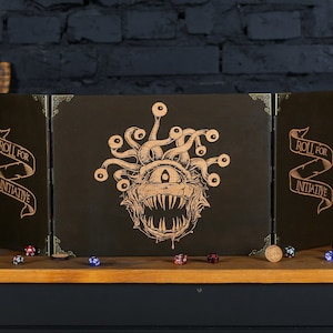 May include: A brown wooden tabletop game screen with a gold trim. The screen is folded in three sections. The center section features a gold illustration of a beholder, a creature with a single large eye and many smaller eyes. The left and right sections have the text "Roll for Initiative" in gold lettering.
