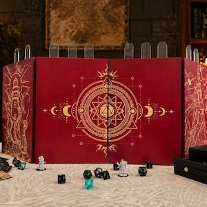 May include: A red tabletop gaming screen with gold geometric designs and clear dividers. Dice, miniatures, and a dice tray are arranged in front of the screen, suggesting a role-playing game theme. The screen has a detailed, ornate design.