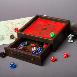 May include: A wooden dice tray with a red felt interior and a drawer. The tray has a circular design with a star in the center. The drawer is open and contains a variety of dice.