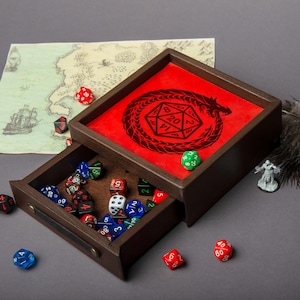 May include: A wooden dice tray with a red interior featuring a black dragon and D20 design. The tray's drawer is open, revealing a collection of colorful polyhedral dice. A map and miniature figure are also visible.