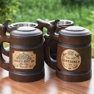 May include: Two dark brown wooden beer steins with metal liners and lids. Each features a decorative handle and a gold-colored metal plaque. One plaque reads "WORLD'S BEST DM WILLIAM" and the other reads "YOU CAN CERTAINLY TRY" with dragon motifs.