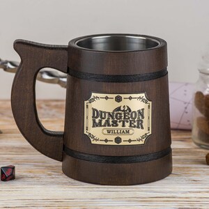 May include: A brown wooden mug with a stainless steel interior. The mug has a black band around the top and bottom and a gold metal plaque with the text "Dungeon Master" and the name "William".