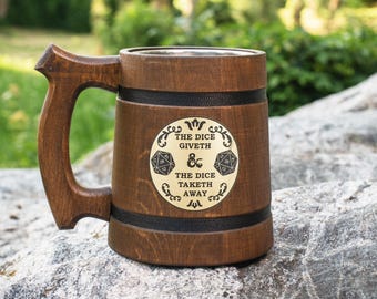 May include: A brown wooden tankard with a large handle and two black bands. A circular gold-colored plaque on the front features the text THE DICE GIVETH THE DICE TAKETH AWAY, flanked by two twenty-sided dice icons and an ampersand symbol.