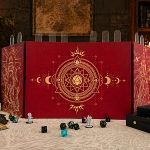 Op de afbeelding: Een rood tabletop gaming scherm met gouden geometrische ontwerpen en doorzichtige verdelers. Dobbelstenen, miniaturen en een dobbelbakje zijn op de tafel geplaatst. Het scherm heeft een zon, maan en sterrenpatroon.