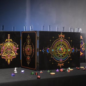 May include: A black four-panel folding game master screen featuring vibrant, multi-colored geometric and celestial designs on the front. The panels are connected by metal hinges and include clear acrylic tabs along the top edge.