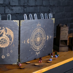 May include: A wooden tabletop gaming set featuring a dragon and dice design. The set includes a folding screen, dice towers, and various dice. The screen is dark with gold accents and a dragon illustration. The dice are scattered on a wooden surface.