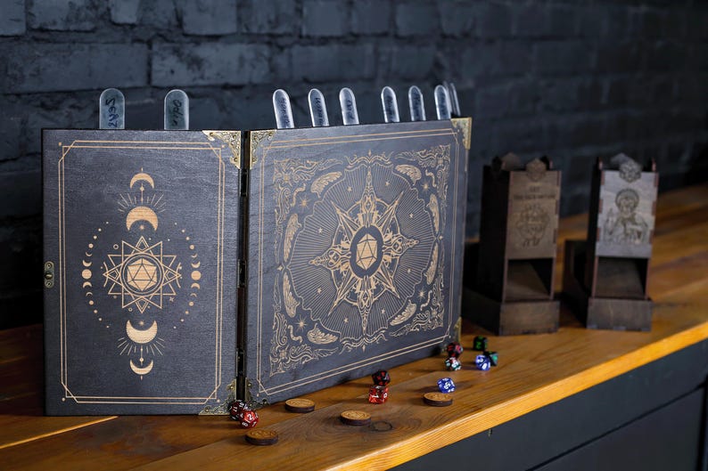 Op de afbeelding: Een donkere houten tabletop RPG-gameset. De set bevat een vouwscherm met hemelse ontwerpen, dobbelsteentorens, dobbelstenen en houten tokens. Het scherm heeft gouden accenten en doorzichtige markeringen.