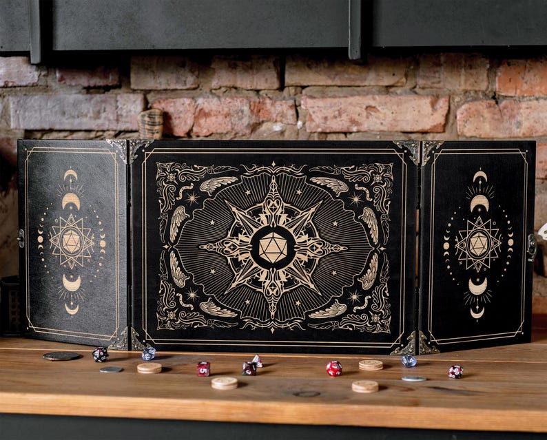 Op de afbeelding: Een zwart, drievoudig spelmeesterscherm met gouden hemelse ontwerpen. Het scherm heeft een centraal sterrenpatroon en maan- en stermotieven op de zijpanelen. Dobbelstenen en fiches liggen verspreid op het houten oppervlak.