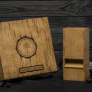 May include: Wooden Dungeons & Dragons dice box and dice tower set. The box features a tree emblem and the words "Dungeons & Dragons". The set is made of light brown wood with a textured, wood-grain appearance. Dice and miniature figures are scattered around the set.