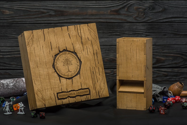 May include: Wooden Dungeons & Dragons dice box and dice tower set. The box features a tree emblem and the words "Dungeons & Dragons". The set is made of light brown wood with a textured, wood-grain appearance. Dice and miniature figures are scattered around the set.