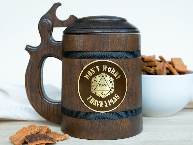 May include: A dark brown wooden beer stein with a lid and a large handle. The stein has a gold emblem with the text "DON'T WORRY FUCK I HAVE A PLAN". A black rope detail wraps around the middle of the stein.