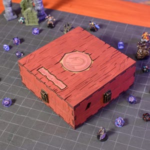 May include: A red wooden box featuring a dragon emblem and the text "DUNGEONS & DRAGONS". The box has a hinged lid and metal clasps. Dice and miniature figures are scattered around the box, suggesting a tabletop game.