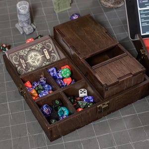 May include: A wooden dice box with multiple compartments, holding various colorful dice and a deck of cards. The box is stained a dark brown and has a hinged lid. The cards have a compass rose design.