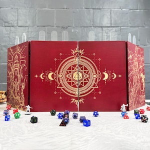 Może przedstawiać: Czerwony ekran do gier stołowych ze złotymi geometrycznymi wzorami i ilustracjami. Ekran ma przezroczyste plastikowe przegrody na górze. Różne kości i miniaturowe figurki są rozrzucone z przodu.