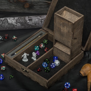 May include: A wooden dice rolling tower and storage box. The box is open, showing a dice tower, dice, miniature figurines, and a map. The dice are various colours and shapes. A wooden pipe rests on the black surface.