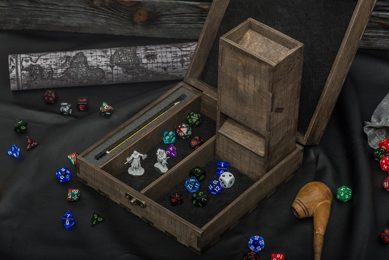 May include: A wooden dice rolling tower and storage box. The box is open, showing a dice tower, dice, miniature figurines, and a map. The dice are various colours and shapes. A wooden pipe rests on the black surface.