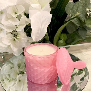 Puede incluir: Un tarro de vela de vidrio rosa con tapa. El tarro tiene un patr&oacute;n de diamante texturizado y la vela es blanca.