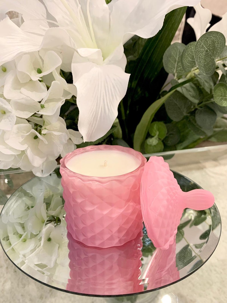 Puede incluir: Un tarro de vela de vidrio rosa con tapa. El tarro tiene un patr&oacute;n de diamante texturizado y la vela es blanca.