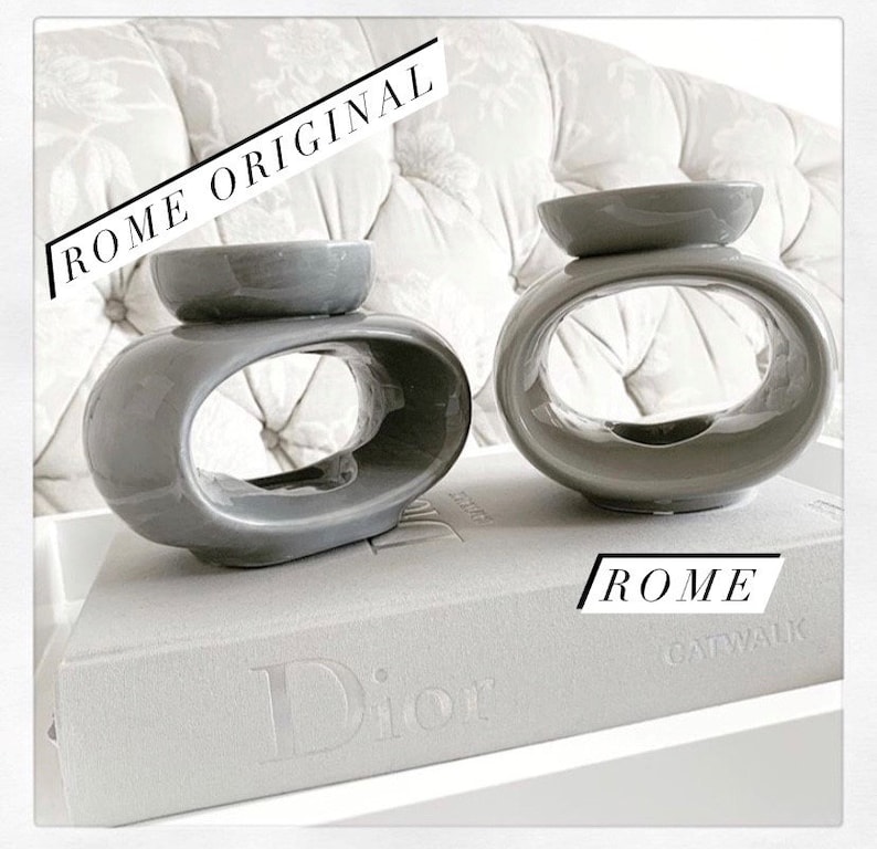 May include: Two grey ceramic oil diffusers with a unique oval design. The diffusers are sitting on a grey book with the word "Dior" printed on the cover.
