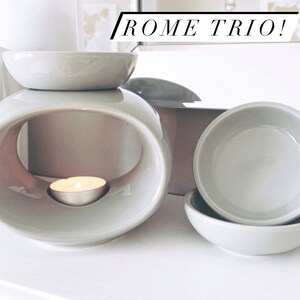 May include: A grey ceramic wax warmer with a round opening and a small tea light candle inside. The warmer is accompanied by two smaller grey ceramic dishes, likely for wax melts. The text "ROME TRIO!" is visible in the background.