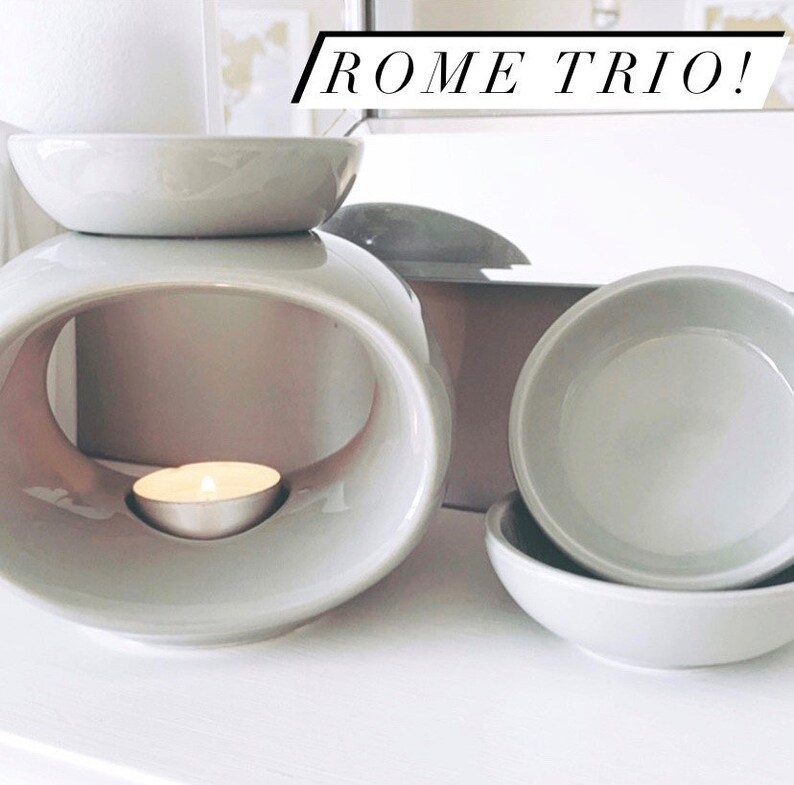May include: A grey ceramic wax warmer with a round opening and a small tea light candle inside. The warmer is accompanied by two smaller grey ceramic dishes, likely for wax melts. The text "ROME TRIO!" is visible in the background.