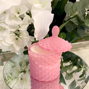 Puede incluir: Un tarro de vela rosa en forma de diamante con tapa. El tarro est&aacute; sobre una superficie de espejo.