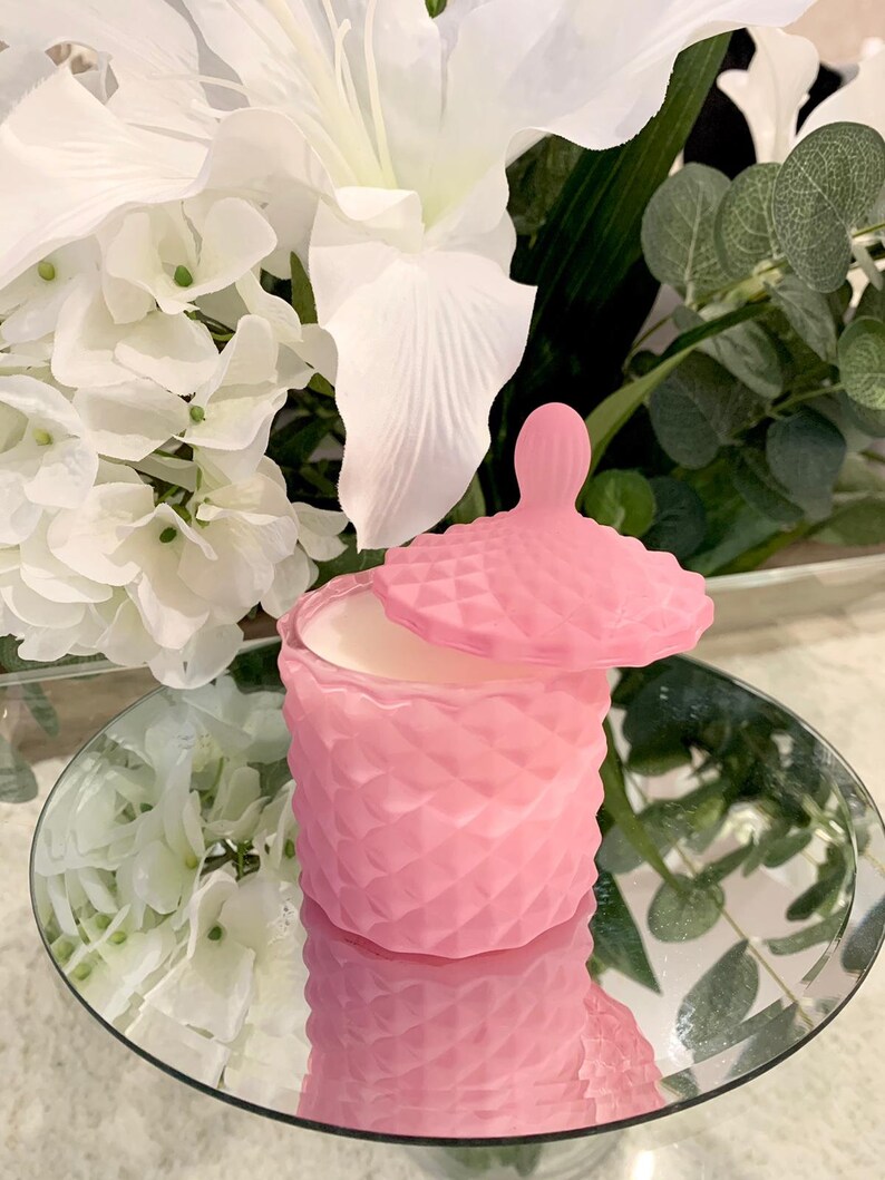 Puede incluir: Un tarro de vela rosa en forma de diamante con tapa. El tarro est&aacute; sobre una superficie de espejo.