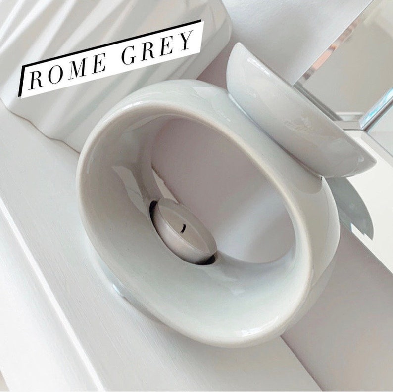 May include: A grey ceramic oil burner with a round, open top and a smaller, round dish on top. The burner has a hole in the side for a tea light candle.
