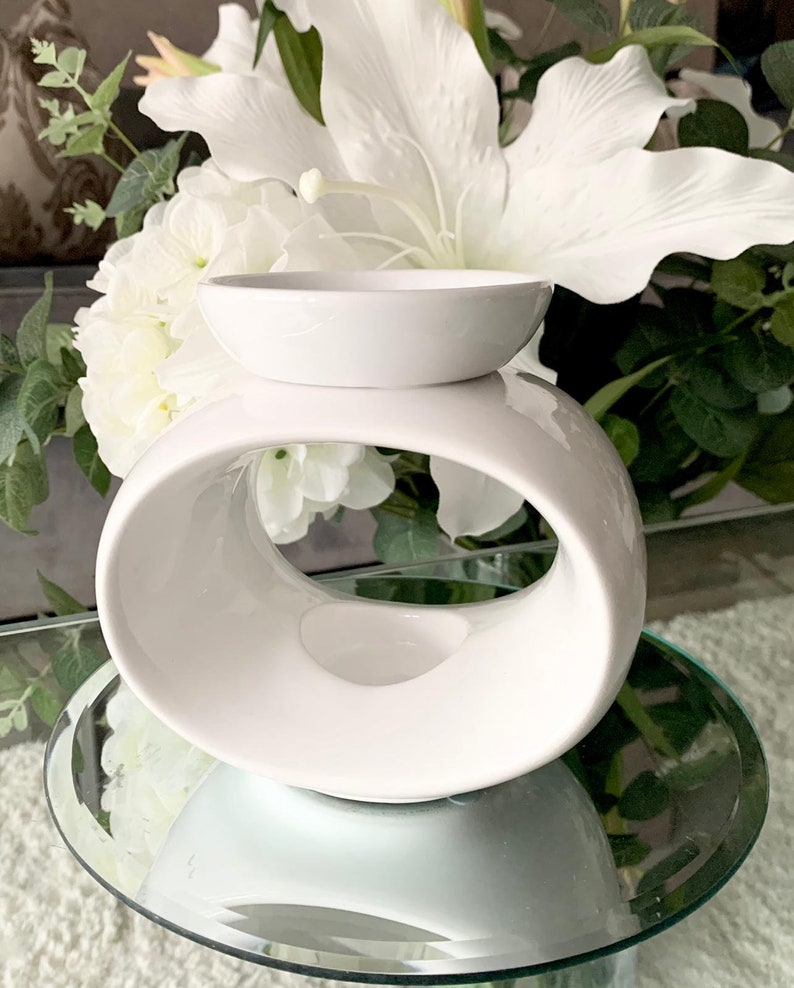 May include: White ceramic wax melt burner with a round, open design. The burner has a small, round dish on top for wax melts.