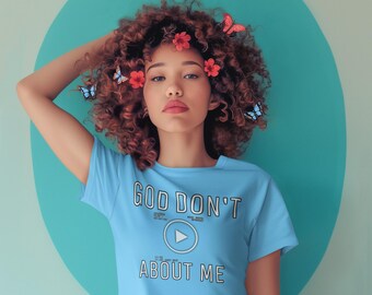 May include: A woman with curly brown hair wearing a light blue crop top with the text "GOD DON'T PLAY ABOUT ME" and a play button graphic. She is wearing blue jeans and has red flowers in her hair.
