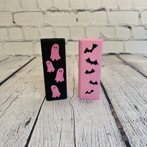 Op de afbeelding: Twee houten blokken, een zwart met roze geesten en een roze met zwarte vleermuizen. Halloween-decoraties.