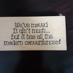May include: A wooden sign with the text "We've moved. It ain't much... but it has all the modern conveniences!"