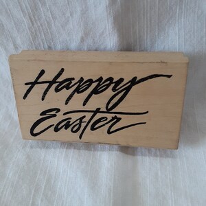 May include: A wooden stamp with the text "Happy Easter" in black script.