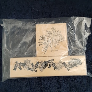 May include: A set of three wooden stamps featuring a Christmas tree design and a holly and pine garland design.