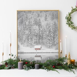 Könnte beinhalten: Ein gerahmter Schwarz-Weiß-Winterlandschaftsdruck mit goldenem Rahmen hängt über einem für die Feiertage dekorierten Kaminsims. Der Kaminsims ist mit Kerzen, Grün und dekorativen Akzenten geschmückt. Ein grüner Kranz hängt an der Wand.