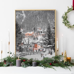 Könnte beinhalten: Ein gerahmter Schwarz-Weiß-Druck eines schneebedeckten Dorfes mit goldenem Rahmen. Der Druck wird über einem Kaminsims mit Grün, Kerzen und Ornamenten ausgestellt. Eine Girlande hängt an der Wand.