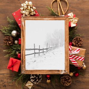 以下が含まれることがあります： 木製のフレームに入った冬の風景シーンで、クリスマスの装飾に囲まれています。 金色のリボンが付いた赤いギフトボックス、松ぼっくり、オーナメントが、常緑樹の枝が付いた木製の表面に配置されています。
