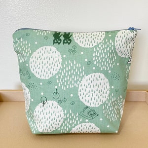 May include: A green zippered pouch with a white and green pattern of raindrops and trees. The pouch features a small black cat illustration and the text "Moomin".