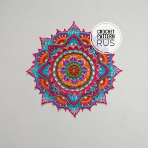 以下が含まれることがあります： ピンク、オレンジ、ブルー、グリーンの繰り返しパターンを持つ、マルチカラーの中心を持つカラフルなクロシェマンダラ。マンダラは白い背景の上にあります。CROCHET PATTERN RUS