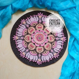 May include: A pink and peach crochet doily with a floral design. The doily is on a brown background and has a white label that says "CROCHET PATTERN ENG/RUS".