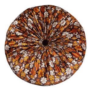 May include: A round, tufted velvet cushion featuring a dark brown base color with a dense, repeating floral pattern in shades of orange, yellow, and white. The fabric radiates from a central, dark brown button tuft, creating deep, uniform pleats.