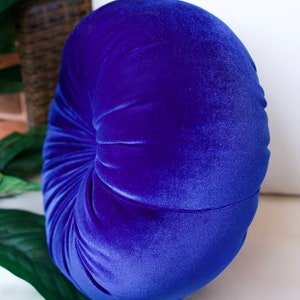 May include: A round, blue velvet pillow with a tufted design. The pillow is soft and plush, perfect for adding a touch of elegance to any room.