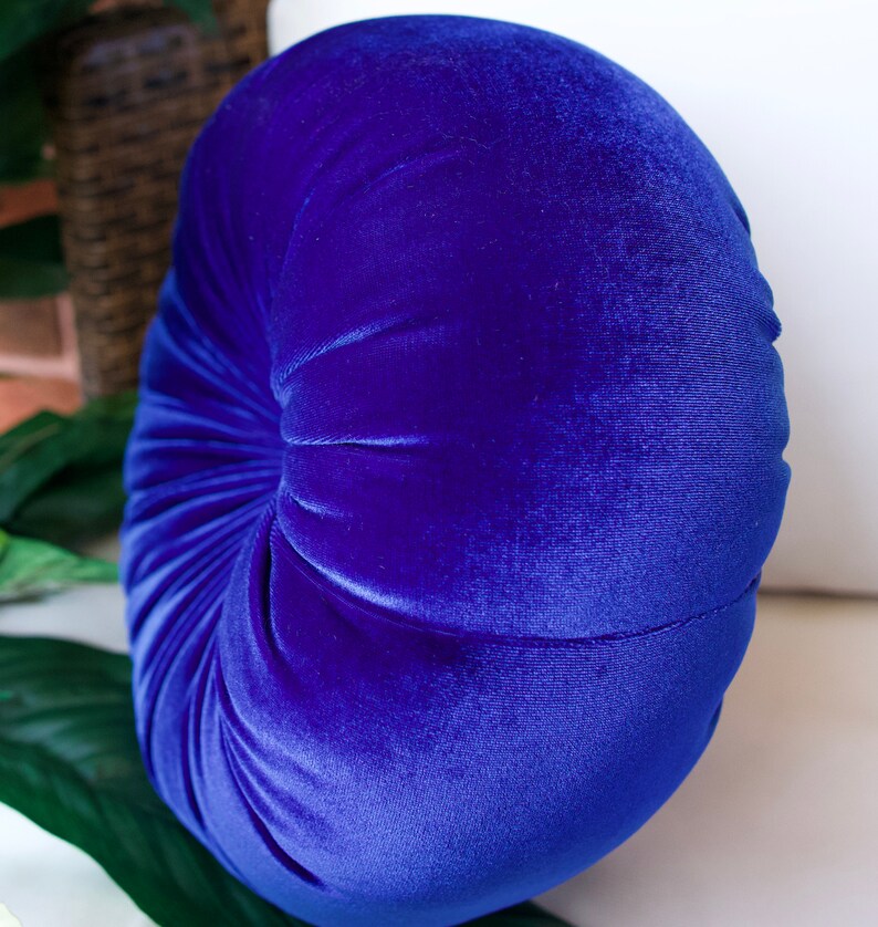 May include: A round, blue velvet pillow with a tufted design. The pillow is soft and plush, perfect for adding a touch of elegance to any room.