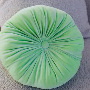 May include: A light green round pillow with a button in the center and a pleated design.