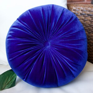 May include: A round, blue velvet pillow with a tufted design. The pillow is soft and plush, and would be a great addition to any living room or bedroom.