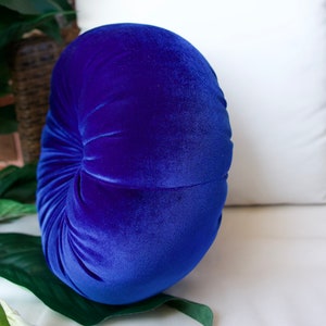 May include: A round, blue velvet pillow with a gathered center. The pillow is soft and plush, and would be a great addition to any home.