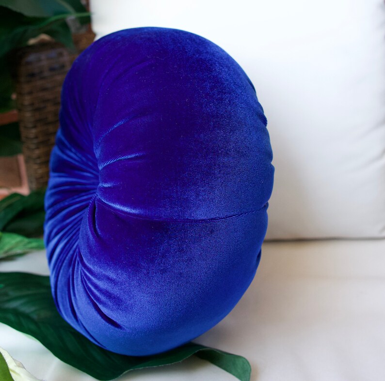 May include: A round, blue velvet pillow with a gathered center. The pillow is soft and plush, and would be a great addition to any home.