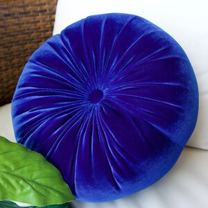 May include: A round, blue velvet pillow with a tufted design. The pillow is soft and plush, and would be a great addition to any living room or bedroom.