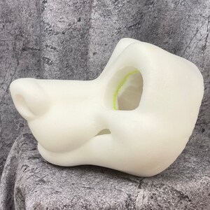 Puede incluir: Base de cabeza de traje de piel de espuma blanca sin terminar con un hocico grande y un solo agujero para los ojos.