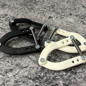 Könnte beinhalten: Zwei schwarze und zwei weiße Klemmen mit Federmechanismen. Die Klemmen sind aus Kunststoff und haben eine U-Form.